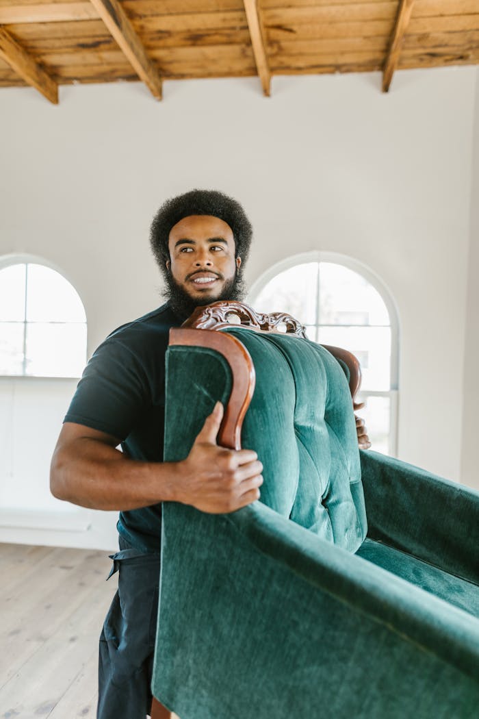 Man in a bright room moving a vintage green armchair with smile.